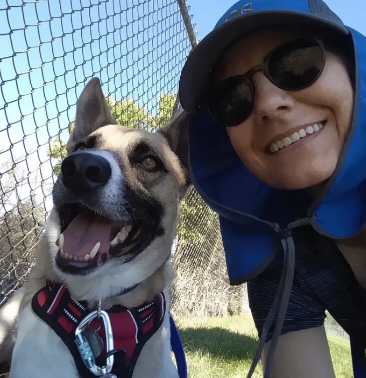 Person smiling with dog by a fence.